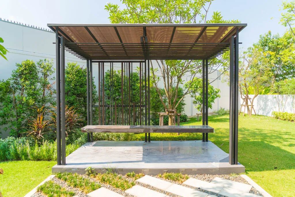 Modern black metal gazebo structure featuring a bench in a landscaped outdoor space.